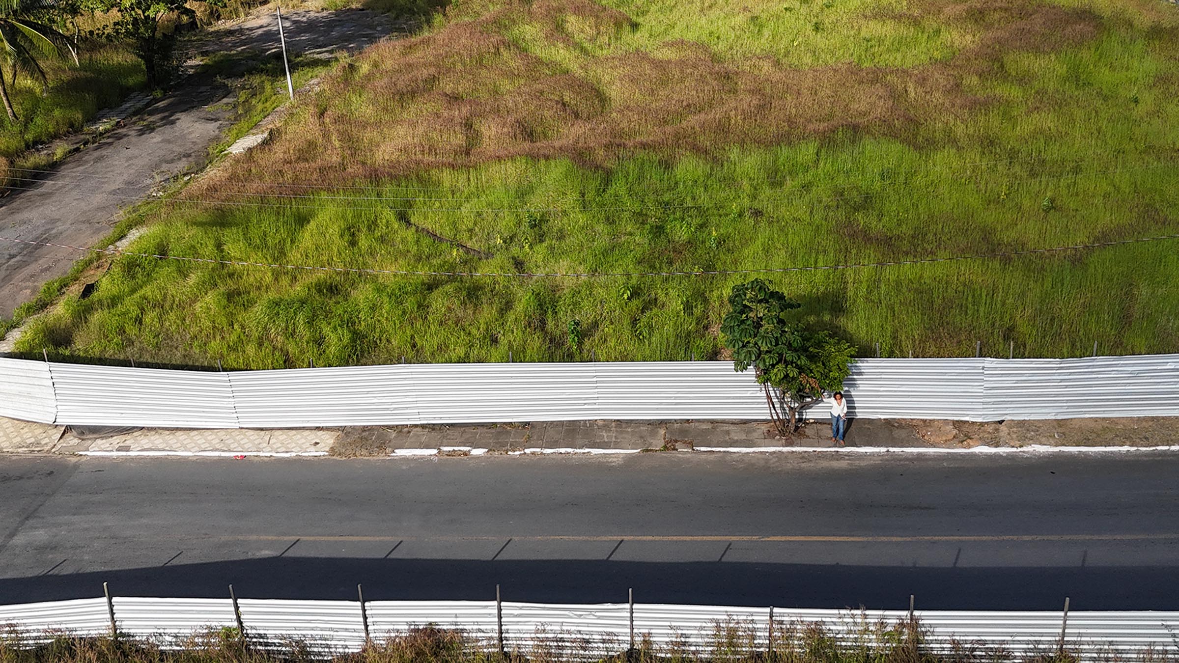 Vista aérea de un barrio de Maceió, con una persona junto a un árbol frente a un terreno cercado