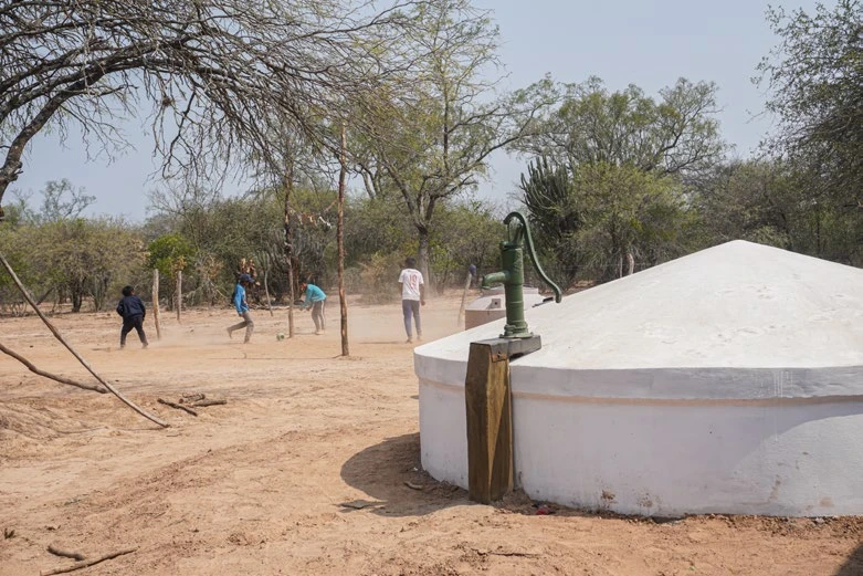 Cisterna de agua con bomba manual y personas jugando en el fondo